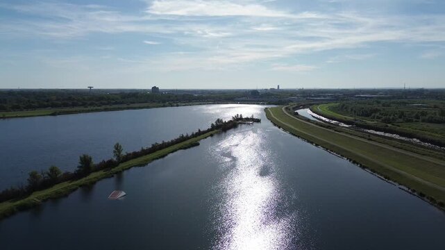 Drone flies southeast over the lake and dike. In the distance: Dijle River, E19 highway and industrial area. A water ski ramp is visible on the lake.