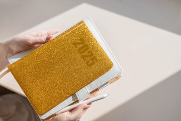 Gold colored diary for the year 2024, pen on bright background. New year planning concept. 