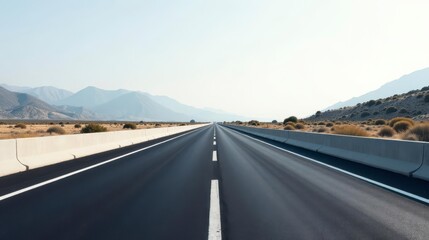 Fototapeta premium Asphalt road stretching towards distant mountains under a clear sky, bordered by low concrete barriers and arid shrubbery