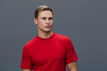 Confident young man with short hair wearing a red t-shirt looks to the side against a plain gray background. Studio portrait, casual style, thoughtful expression, male model, natural colors