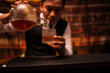A bartender stands pouring whiskey for customers.
