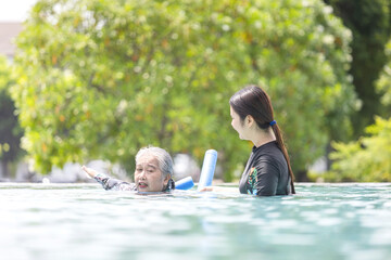 Water Therapy and Exercise, Senior Woman Swimming and Exercising with a Young Instructor, Female Coach Teaching an Asian Senior to Swim or Do Pool Aerobics
