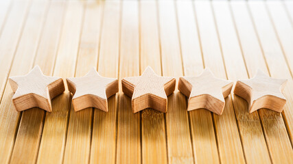 Five wooden stars aligned on bamboo wooden surface. Symbol of high rating, customer satisfaction,...