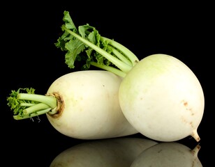 Two white radishes with green tops on black background