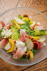 Colorful salad with mixed greens, slices of apple, and cured meats on a rustic wooden table