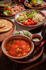 A vibrant bowl of soup with herbs sits among various enticing dishes on the wooden table