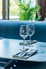 Two crystal wine glasses rest beside silverware on a stylish table, surrounded by greenery