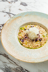 A creamy risotto with microgreens and cheese rests on a marble table at a cozy restaurant