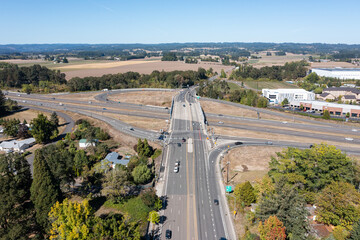 Aerial drone picture of traffic on US 26 highway in Hillsboro Oregon during a clear fall day, showing multiple lanes of cars and trucks moving under blue sky with surrounding suburban and rural are