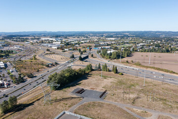 Aerial drone picture of traffic on US 26 highway in Hillsboro Oregon during a clear fall day, showing multiple lanes of cars and trucks moving under blue sky with surrounding suburban and rural are