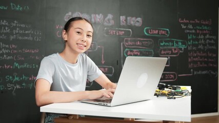 Smart girl programming system by using laptop at blackboard. high school student writing engineering code or prompt while looking at camera at STEM technology class. Creative education. Edification