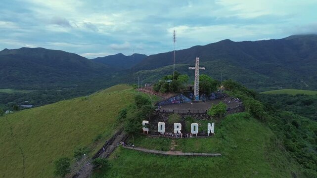 Wide aerial view of Mount Tapyas cross and CORON hillside letters surrounded by green ridges and cloudy evening mountains in Coron Palawan