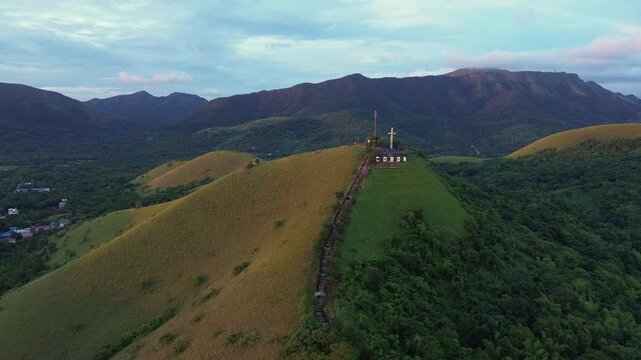Long aerial view of Mount Tapyas ridge with CORON letters white summit cross and stairway leading across green hills toward forested mountains