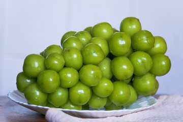 Large Korean grapes. A bunch of green grapes lies on a white plate; the berries are large, smooth, glossy, and a rich light green. The background is light, and the plate sits on a wooden surface.