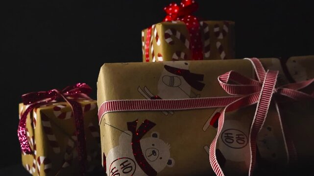Close up video gliding over beautifully wrapped Christmas presents and holiday gifts with long ribbons and cany cane and holiday spirit decorations in front of a black studio background.