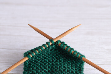 Close-up of green garter stitch knitting with crossed wooden needles on light gray table. Horizontal minimalist background with copy space. Concept of knitting craft and DIY inspiration