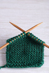 Vertical fragment of green garter stitch knitting with wooden needles on gray surface. Minimalist style with neutral background and copy space. Concept of handmade crafts and slow living