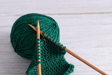 Green yarn ball with garter stitch fabric and wooden knitting needles on light gray wooden background. Horizontal minimalist image with copy space. Concept of knitting craft and handmade lifestyle