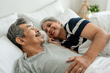 Fototapeta premium Asian elderly older couple lying down on bed, talking to each other. 