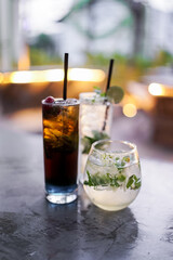 Three refreshing mocktail drinks in glass cups with ice and straws on a marble table during sunset at an outdoor cafe, showcasing vibrant and colorful tones.