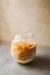 Minimalist shot of iced coffee with milk served in a round glass on a textured table, showing beautiful coffee swirl and soft lighting.