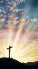 Silhouette of cross on hill at sunrise with dramatic rays of light shining through clouds