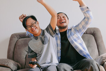 Father and Son Celebrating Video Game Victory With Raised Arms and Smiles in Home