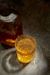 Bottle and crystal glass of whiskey on a old stone table.