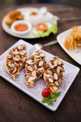 Selective focus of almond croissant with chocolate drizzle served on a white plate with strawberry garnish. Dessert pastry for coffee shop or breakfast menu.