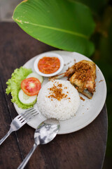 Indonesian fried chicken with white rice, sambal chili sauce, and fresh vegetables served on a plate. Traditional Asian lunch menu with local spices