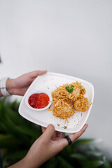 Fried noodle balls served with chili sauce on a white plate. Crispy Indonesian snack made from noodles, perfect for appetizer or street food photography.