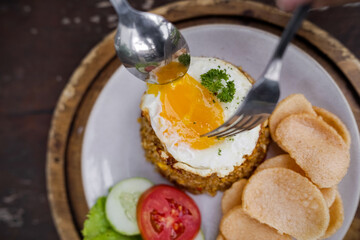 Indonesian fried rice served with sunny side up egg, fresh vegetables, and crackers on a rustic wooden table, traditional Asian cuisine.