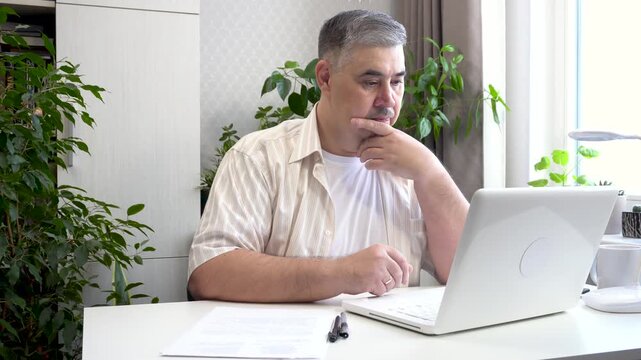 Close-up footage of a male freelancer working from home on a computer. Captures him typing on a keyboard and then contemplating while looking at the screen. Suitable for content about freelancing and 