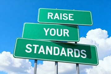 Motivational road sign featuring the message 'RAISE YOUR STANDARDS' displayed prominently against a clear blue sky with fluffy white clouds.