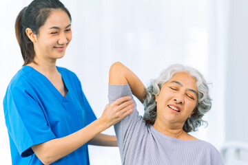 Fototapeta premium Young nurse trains elderly woman to exercise her arm during therapy and rehabilitation in her living room at home. Physical therapist.