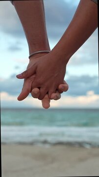 Romantic couple slowly holding hands on the beach