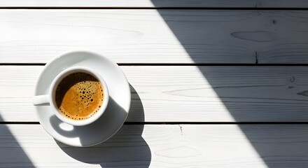Top view of fresh espresso coffee cup on white wooden planks with harsh diagonal shadows.