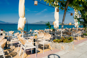 Sunny outdoor terrace of a seafront café in, Central Greece. Elegant wicker chairs, tables, and...