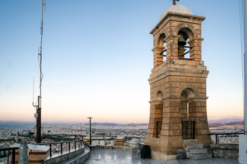 Scenic view of the bell tower of Saint George Church on Lycabettus Hill in Athens, Greece. The stone tower stands on the hilltop with a panoramic view of the Greek capital spreading into the distance