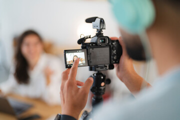 A male videographer films a young woman for a professional video project. He adjusts the camera settings on the screen, ensuring the shot is perfect for content creation.
