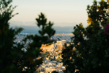 View of Athens with the Acropolis and Parthenon illuminated by the warm light of sunsrise. The historic ancient citadel rises above the modern city, 