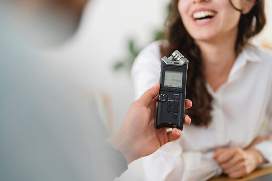 A person holds a digital audio recorder, capturing the laughter of a woman during an interview or conversation.