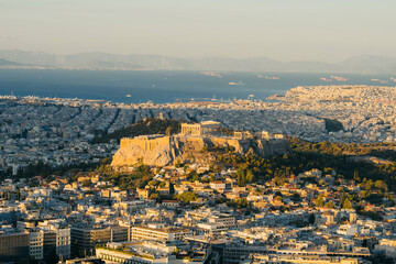 View of Athens with the Acropolis and Parthenon illuminated by the warm light of sunsrise. The historic ancient citadel rises above the modern city, 