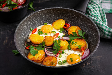 Fried eggs and potatoes with onions and chili peppers in a dark background.
