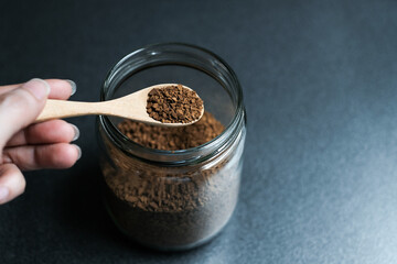 Instant coffee and spoon above glass jar on grey table, top view.