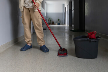 Person mopping a clean floor in a hallway with plants and bright walls during daylight hours