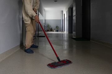 Person cleaning a hallway floor with a mop in an apartment building during daylight hours