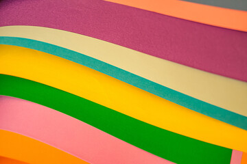 Abstract background of colorful paper sheets layered in waves. Showing vibrant tones of pink, green, yellow, blue, orange and purple with smooth textures. Selective focus.