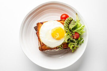 Toasted sandwich with sunny-side-up egg and fresh salad on white plate. Minimalist food presentation, top view, isolated on white background.
