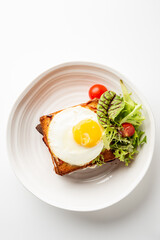 Toasted sandwich with sunny-side-up egg and fresh salad on white plate. Minimalist food presentation, top view, isolated on white background.